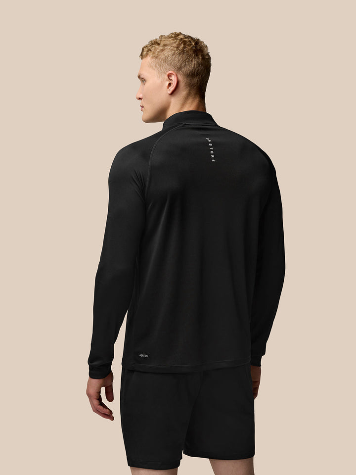 Back view of male model in black Adapt Training 1/4 Zip Top showing vertical branding on the upper back and Aertek logo near the lower back.