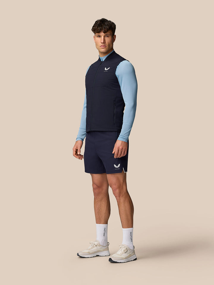 Male model wearing navy Apex Training Gilet over a light blue top with navy shorts