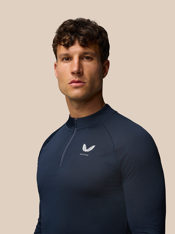 Close-up of navy quarter zip top featuring the Castore logo on the left chest and zip neck detail