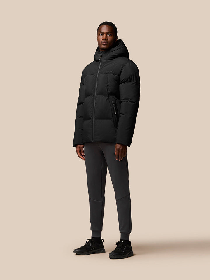 Male model in black hooded puffer jacket with front zip and zipped pockets, Castore branding on chest.