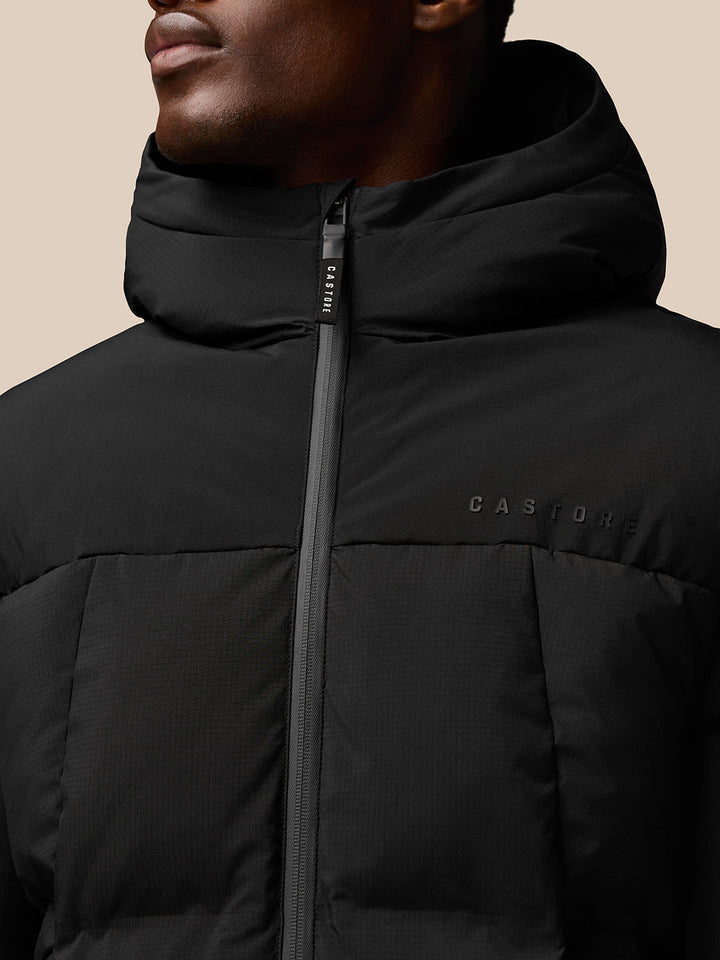 Close-up of black Castore puffer jacket with front zipper and hood, chest logo and ProTek branding on the sleeve