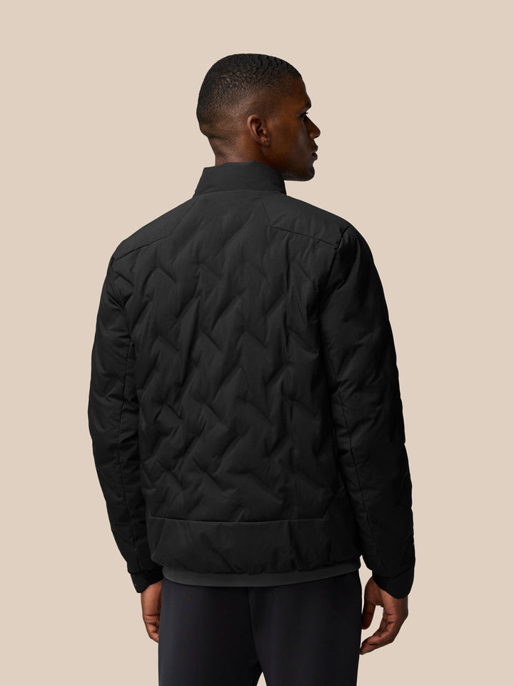 Back view of a man wearing the black padded jacket showing quilted panels and ribbed hem