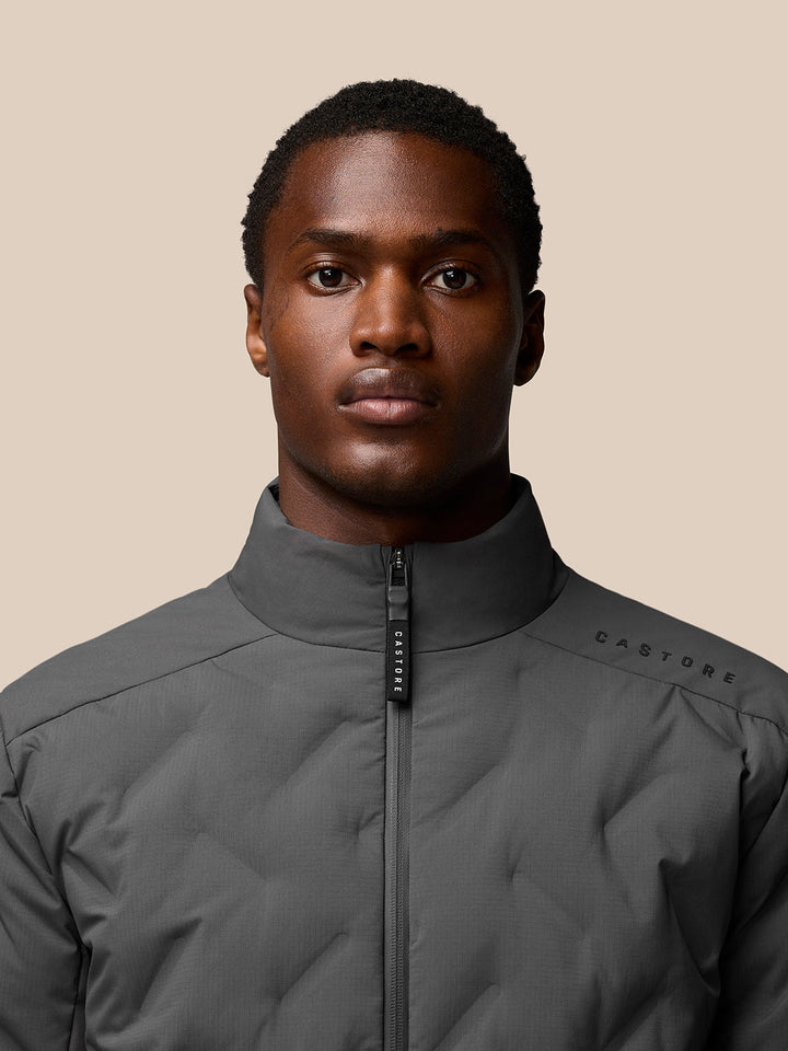 Close-up of charcoal Quilts Lifestyle Jacket showing stand collar and zip with Castore branding on shoulder.