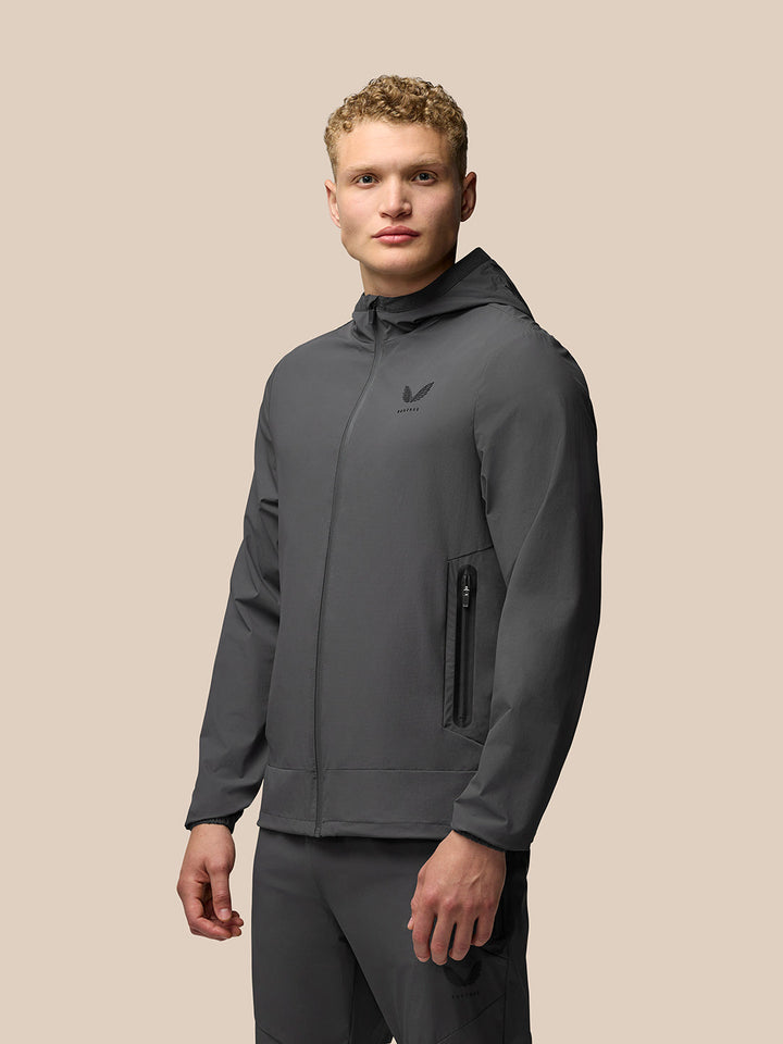 Male model in charcoal Lightweight Flex Jacket with hood and zip pockets.