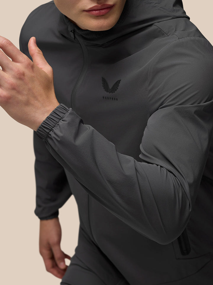 Full-body profile of male model in charcoal Lightweight Flex Jacket with hood down and front zip