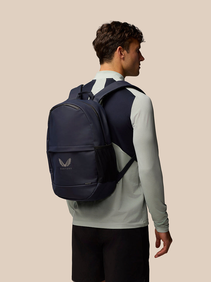 Man wearing a navy backpack with padded back and a front pocket against a beige background