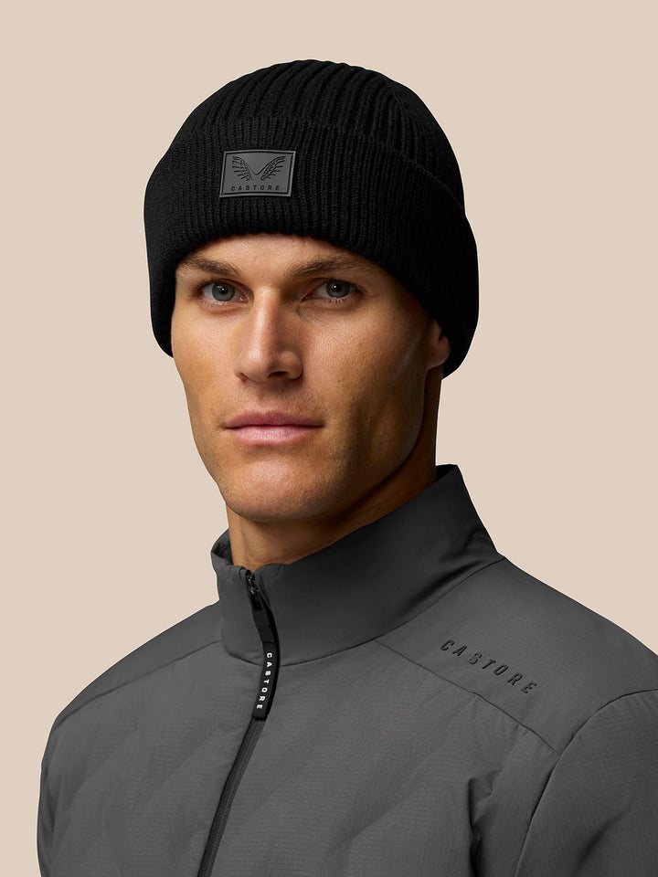 Male model wearing black ribbed Castore Active Beanie with front logo patch.
