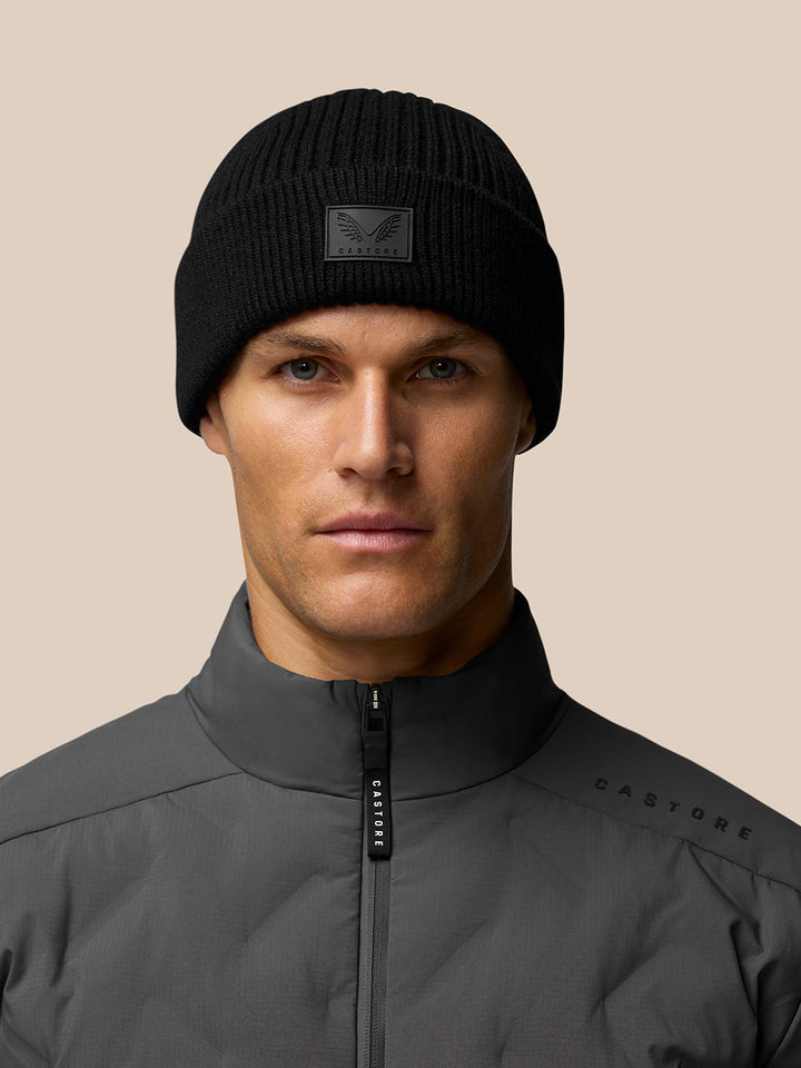Male model wearing black ribbed Castore Active Beanie with front logo patch and grey outerwear.