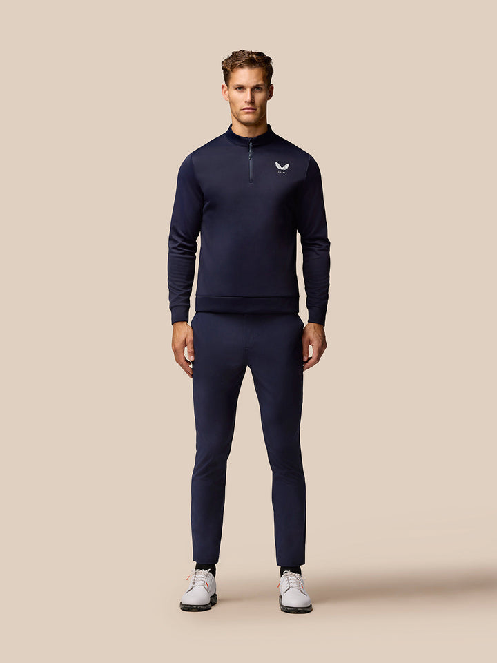 Full body view of a man in navy golf outfit with a zip neck top and matching trousers.