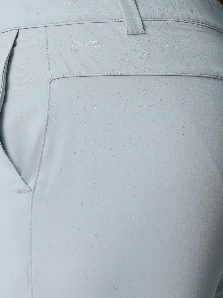 Close-up of light grey golf shorts fabric with water droplets and ProTek branding at the waistband.