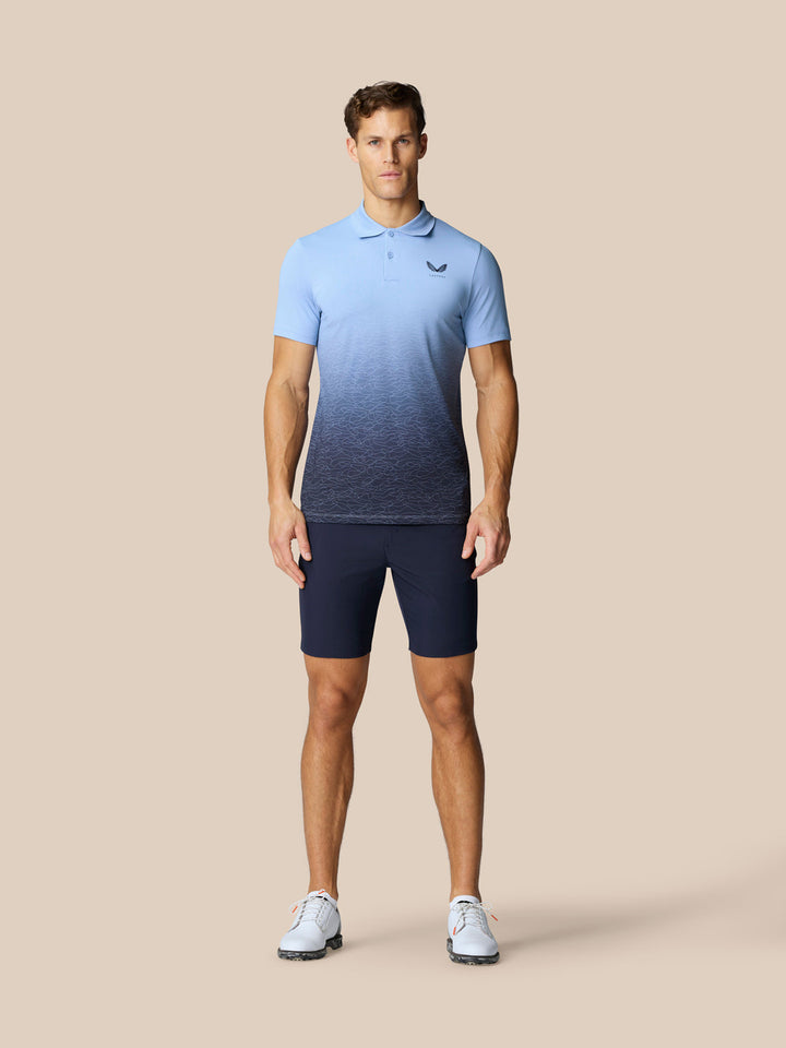 Male model wearing navy golf shorts and a light blue gradient polo on a beige background