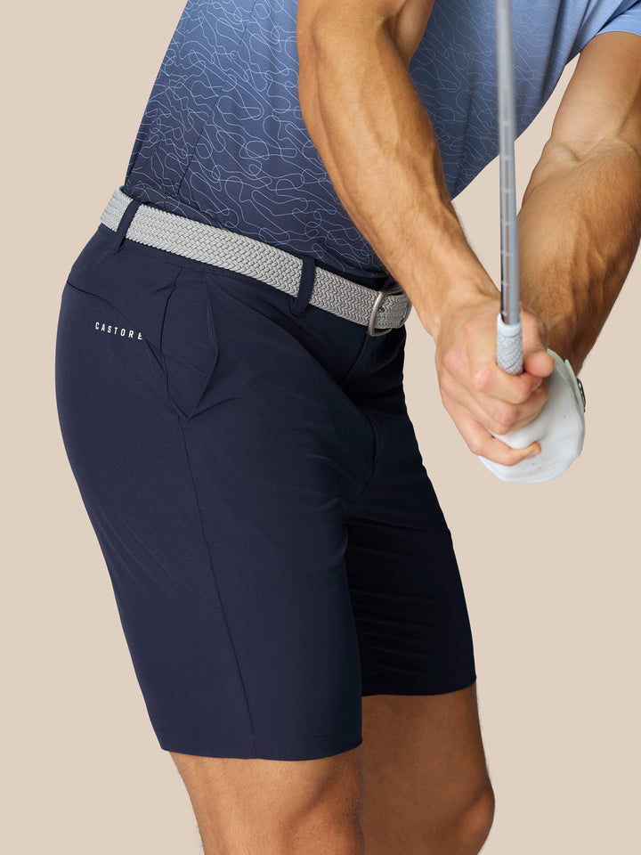 Close-up of navy golf shorts with a light gray woven belt, Castore branding on the thigh and rear, and ProTek branding at the left rear waistband.