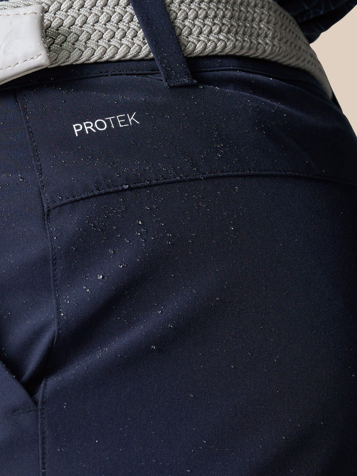 Close-up of navy golf shorts waistband area with ProTek branding and water droplets on the fabric.
