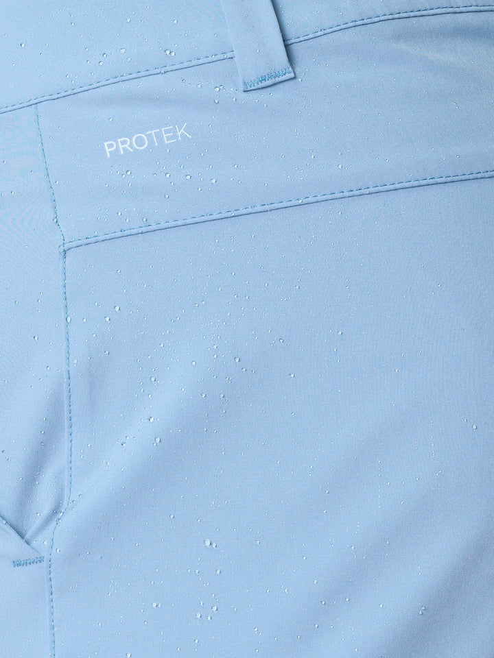 Close-up of sky blue golf shorts fabric with water droplets and a belt loop showing ProTek branding