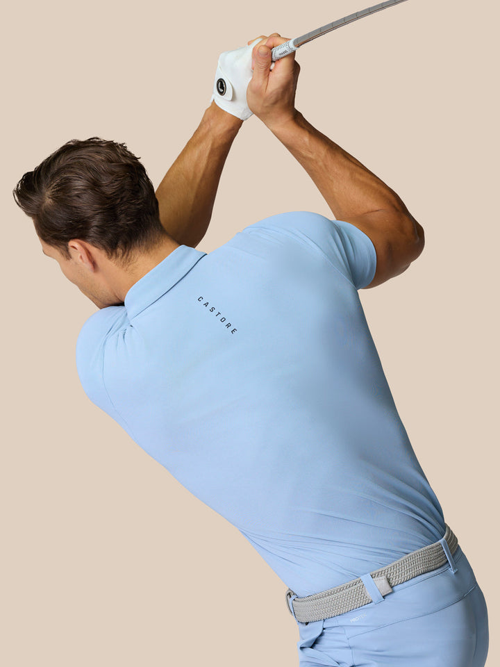Golfer in a sky blue Golf Club Essential Polo mid swing with Castore logo visible on the back.