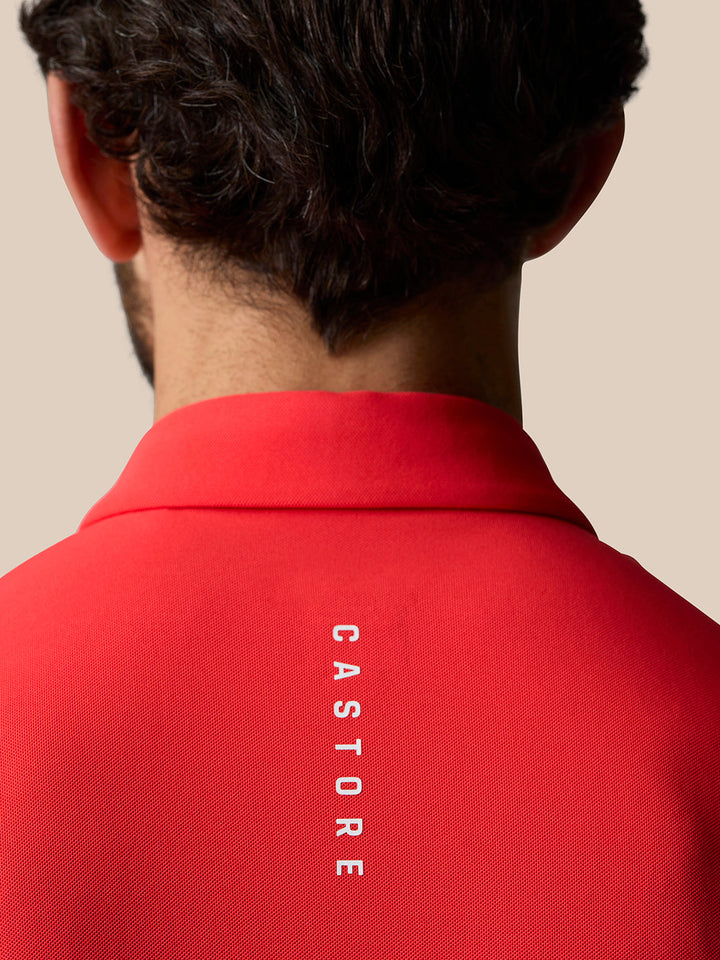 Back view of a man wearing a red Poppy Castore golf polo with vertical branding along the back.