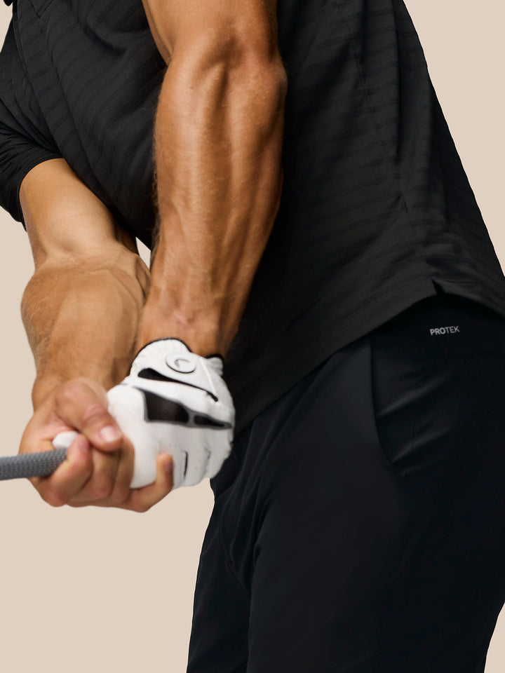 Back view of a man in a black striped golf polo with Castore branding on the upper back.