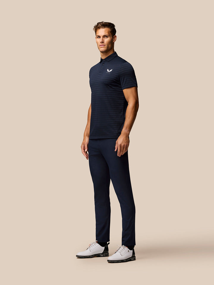 Male model in navy Pinnacle Pique Stripe Polo with Castore logo on chest, paired with navy shorts.