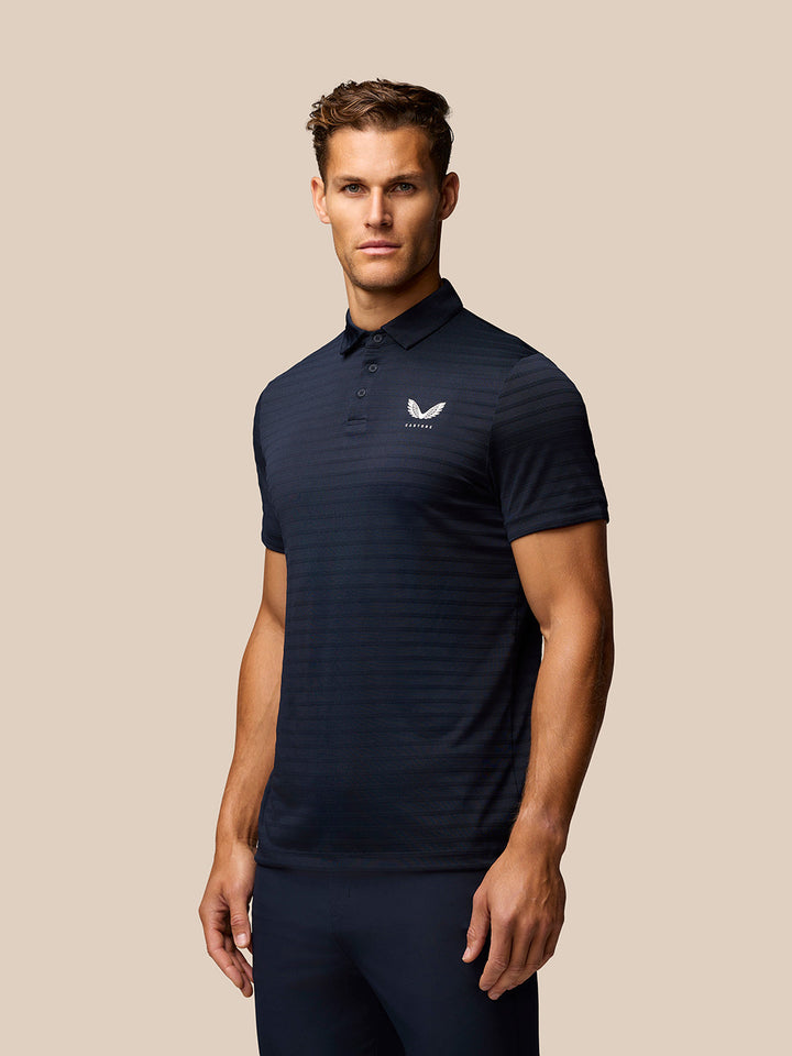 Male model wearing navy Pinnacle Pique Stripe Polo with chest logo, posing.