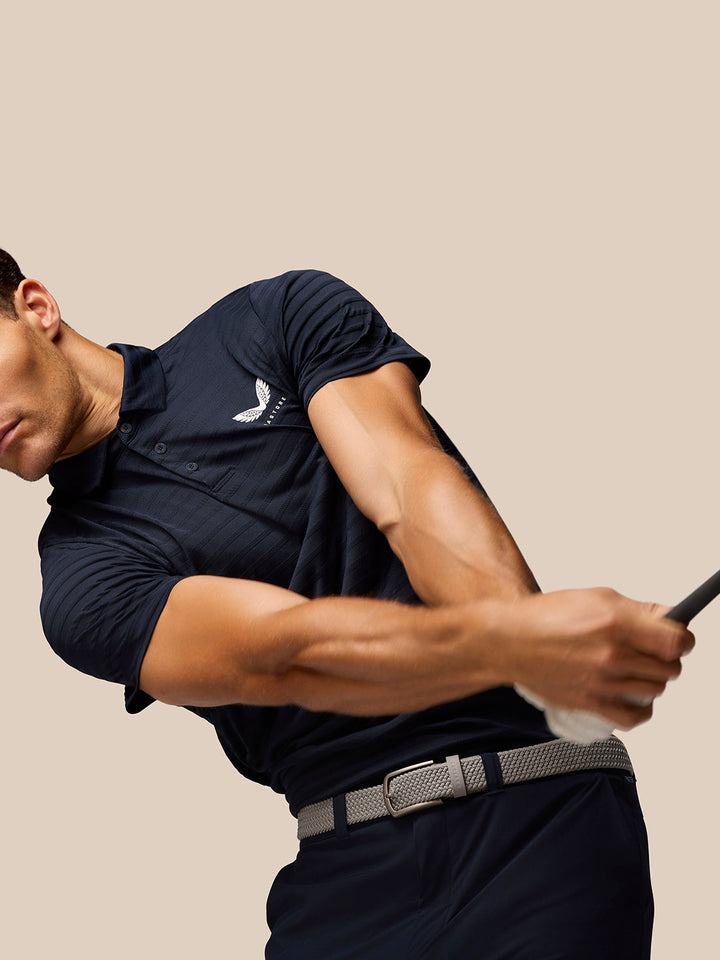 Male golfer in navy Pinnacle Pique Stripe Polo with Castore logo mid swing.