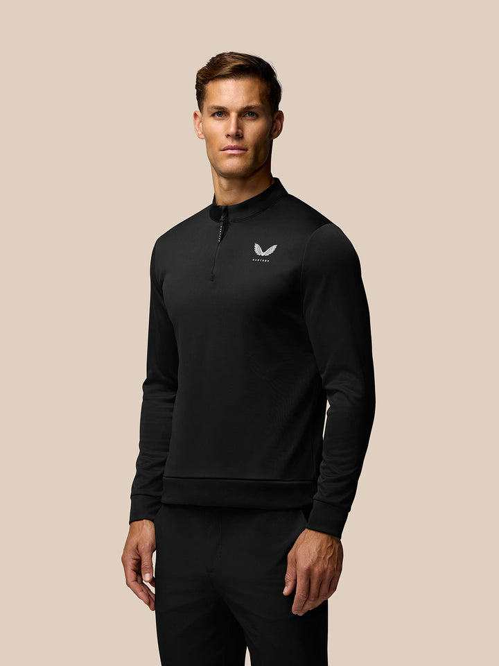 Male model wearing black long sleeve golf top with stand collar and front quarter zip Castore logo on left chest