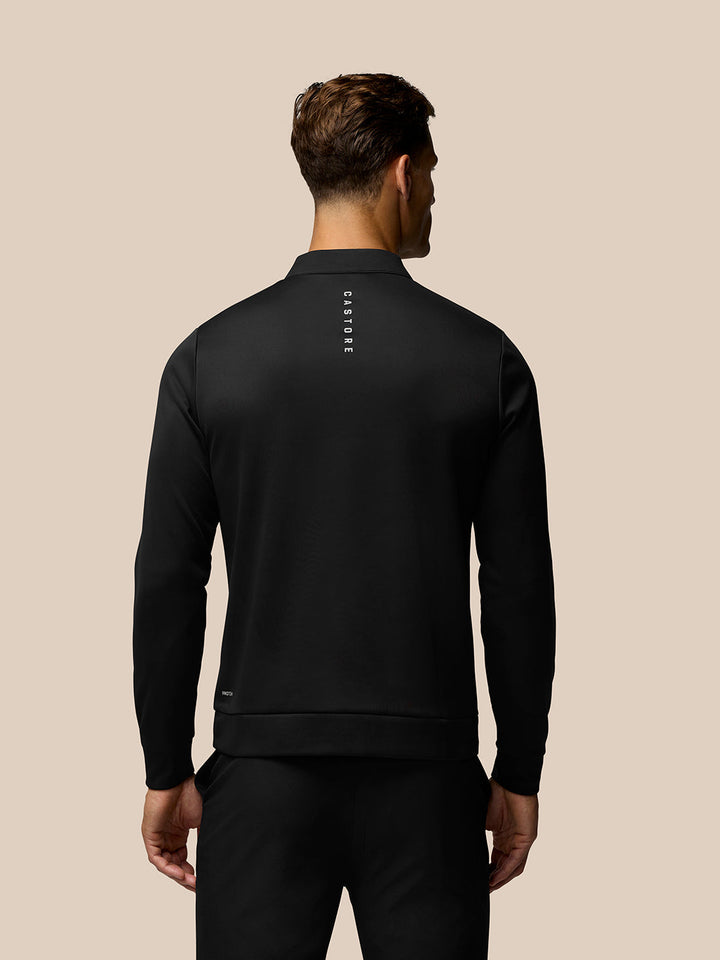 Back view of black long sleeve golf top showing vertical Castore branding down the spine and Protek logo at lower back