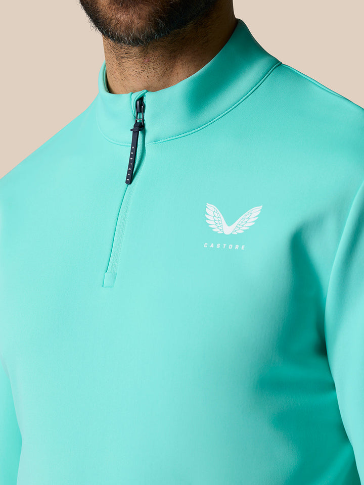 Close-up of light aqua Castore golf quarter-zip top showing stand collar and left chest logo