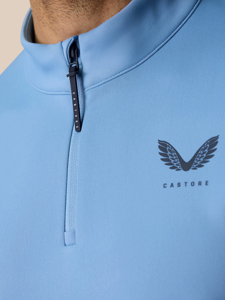 Close-up of light blue Golf Club Classic Quarter Zip Top showing a CASTORE zip pull and wing logo on the chest.
