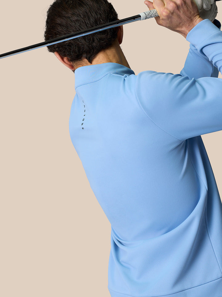 Back view of a golfer wearing a sky blue Golf Club Classic Quarter Zip Top with a high collar and CASTORE branded zipper pull.
