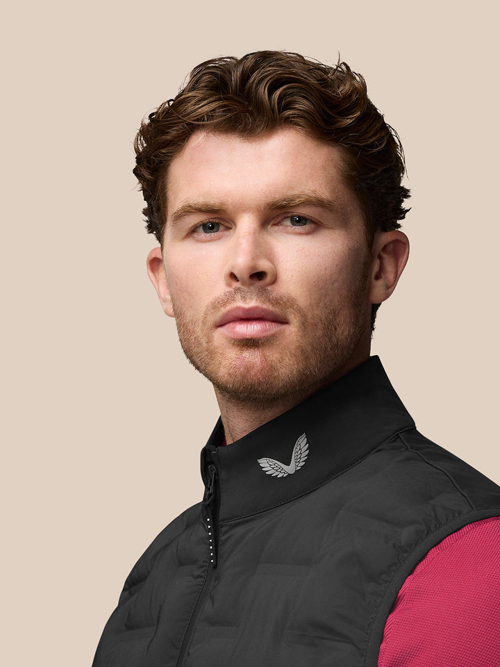 Profile of male model wearing black Golf Pinnacle Gilet with logo on the collar and zip detail