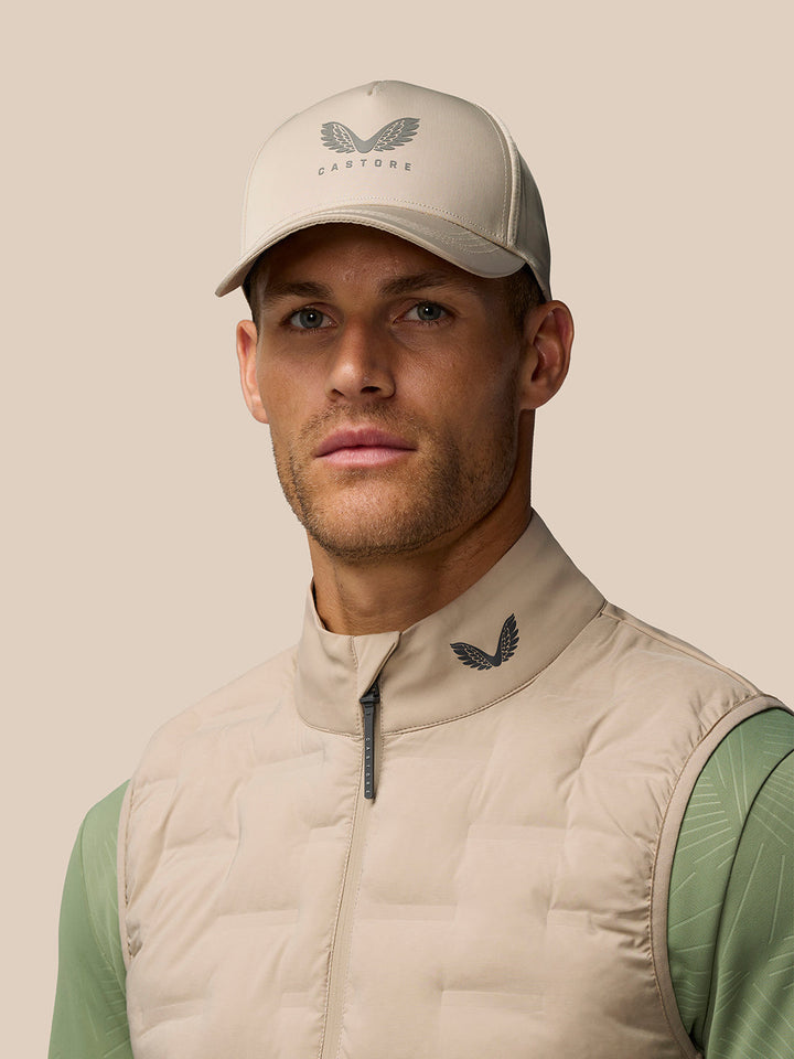 Man wearing mushroom golf gilet with quilted front and funnel collar, Castore logo at the collar, beige backdrop