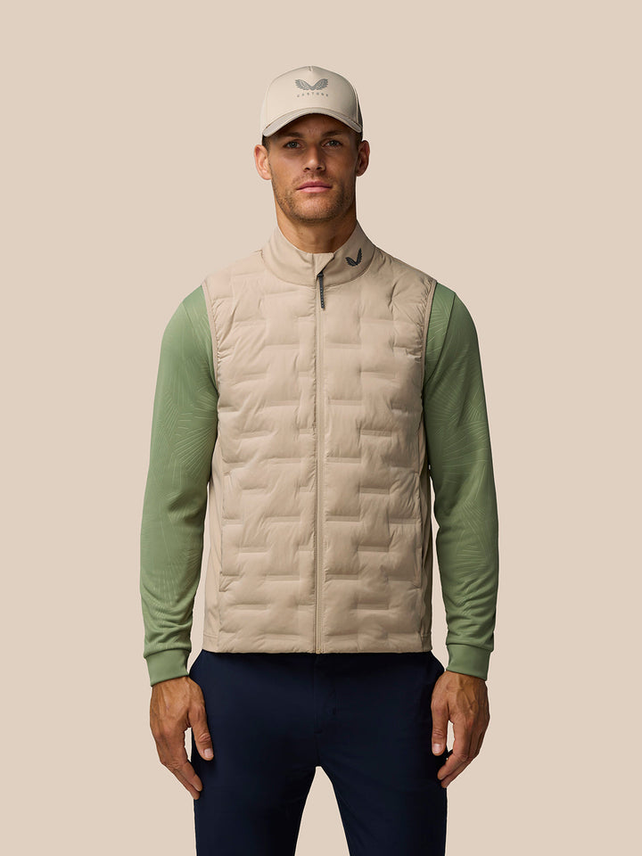 Man wearing mushroom Pinnacle lightweight hybrid gilet with cap featuring Castore logo and green sleeves visible