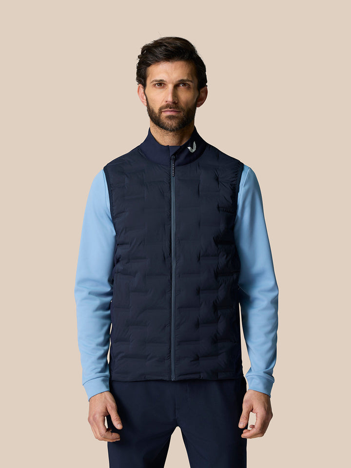 Front view of a man wearing a navy Pinnacle Gilet over a light blue top, featuring a stand collar and full front zip