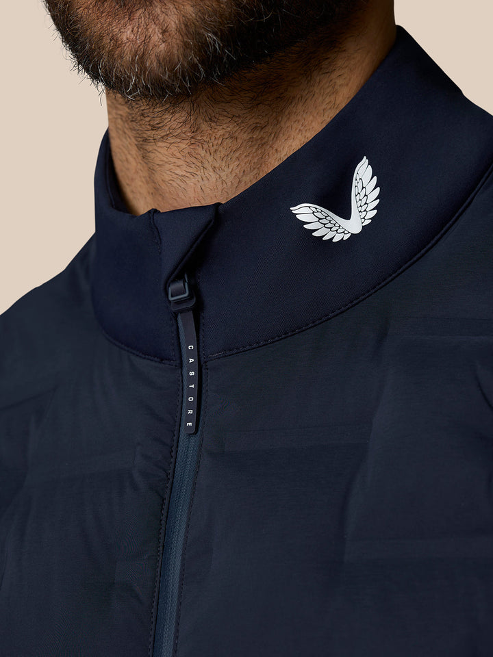Close-up of the navy Pinnacle Gilet collar showing the Castore wing logo and the zip pull