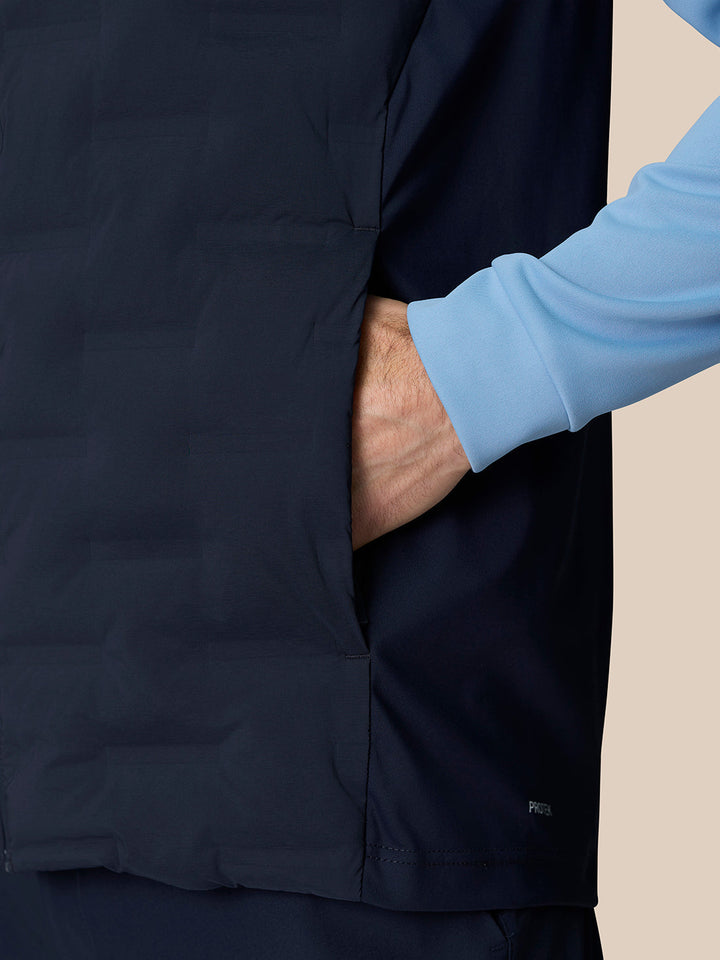 Side view of navy gilet with hand in pocket and blue underlayer sleeve, Protek branding at the hem.