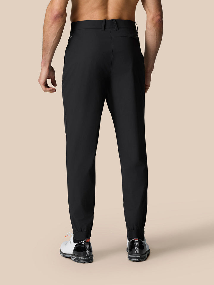 Rear view of male model in black Castore Golf Pinnacle 32 trousers with belt loops and cuffed ankles