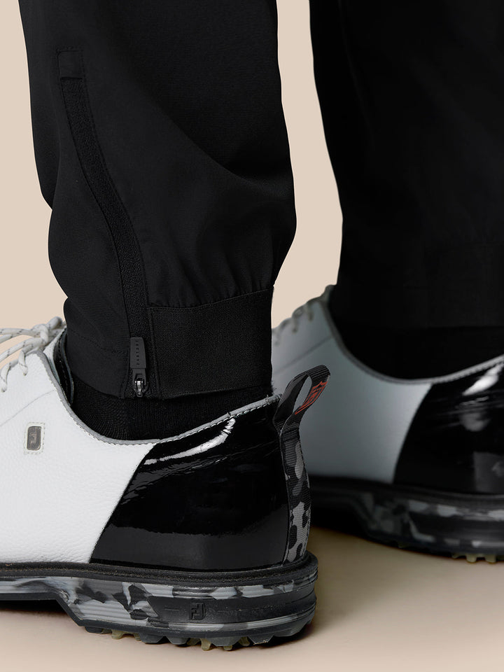 Close-up of black Golf Pinnacle 32 trousers ankle area with lower leg zipper and strap detail, worn with a white trainer.
