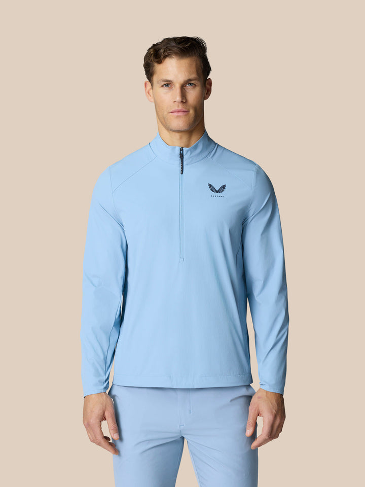 Male model in sky blue Golf Flex Jacket with high funnel neckline and half zip front; Castore graphic on left chest