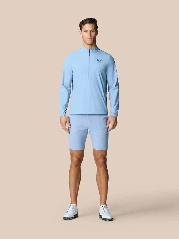 Male model wearing sky blue Castore Golf Flex Jacket with half zip front and left chest logo.