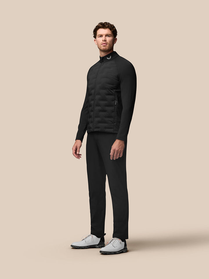 Male model wearing black Golf Pinnacle Jacket with quilted front, paired with black trousers and white golf shoes.