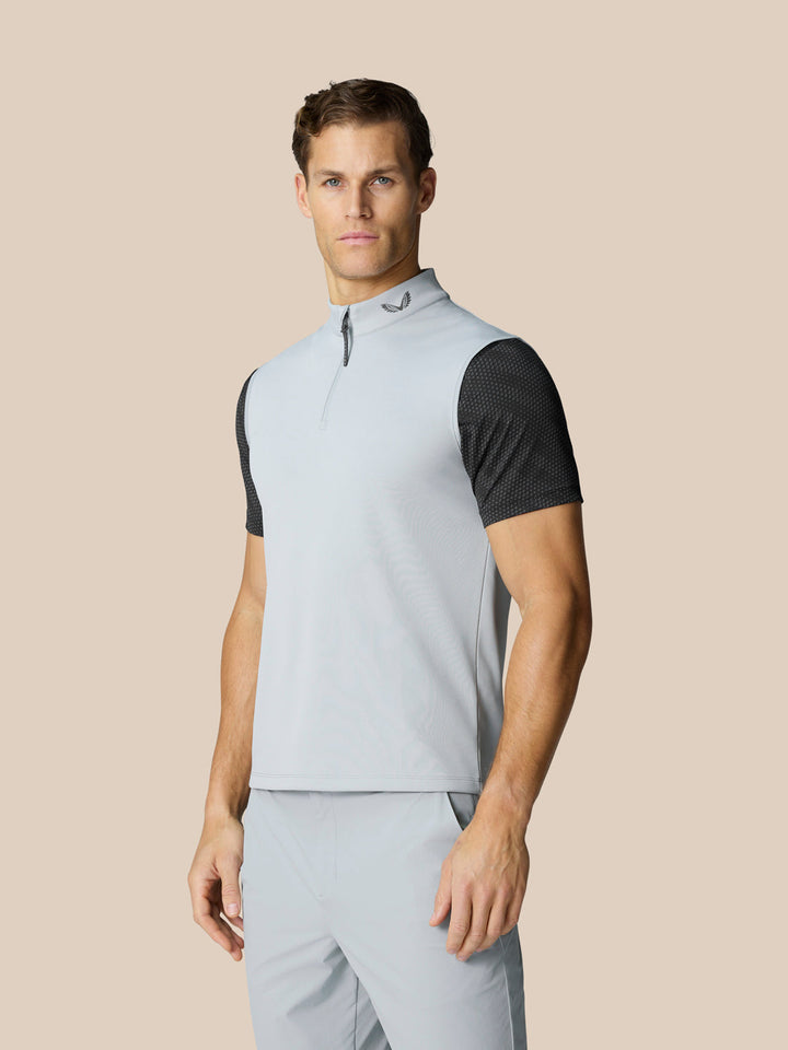 Male model wears light grey sleeveless golf gilet with high collar and half zip over a black mesh tee.