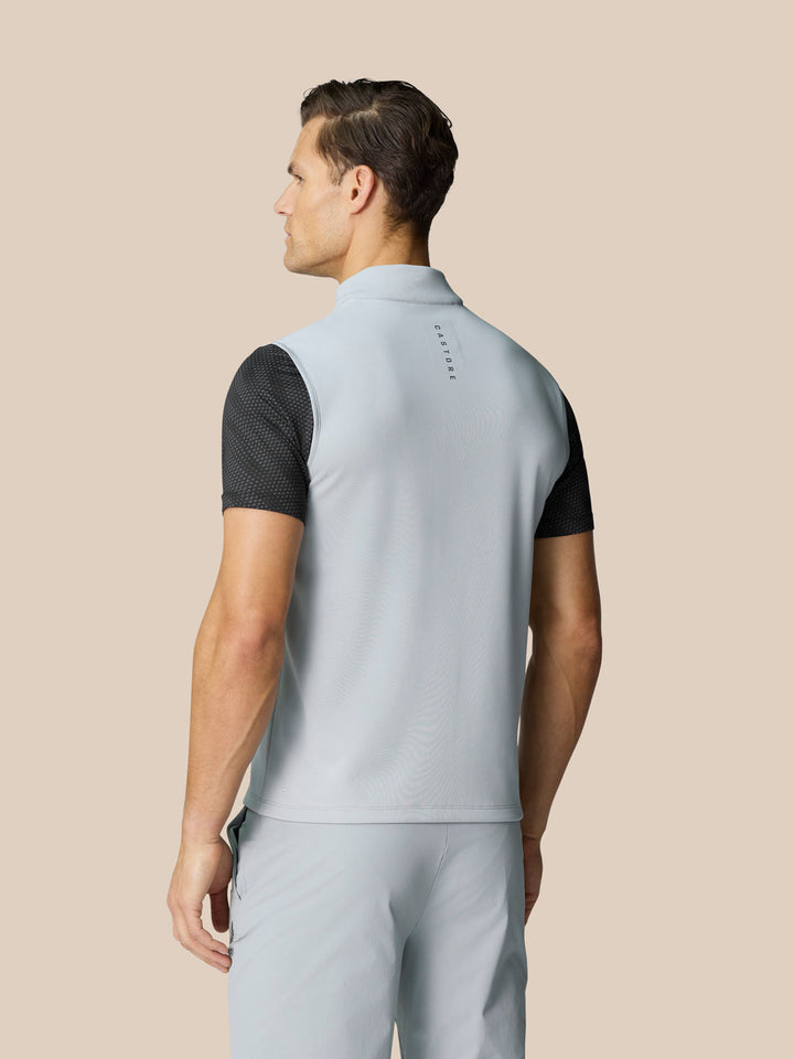 Back view of light grey sleeveless golf gilet worn over a black dotted tee with Castore branding down the back.