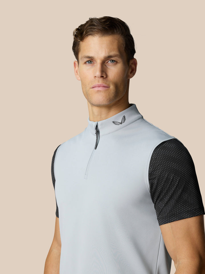 Portrait of a man in a light grey half zip golf gilet with logo on the collar and black mesh sleeves visible.