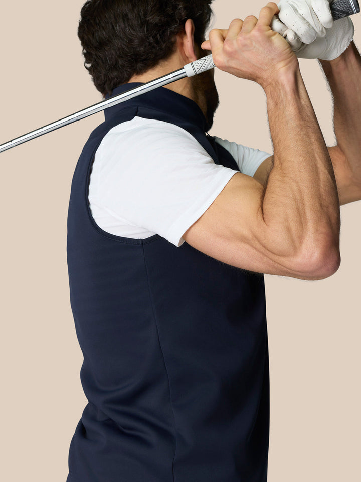 Male model wearing navy 1/2 Zip Gilet with high neck and sleeveless design, holding a golf club.