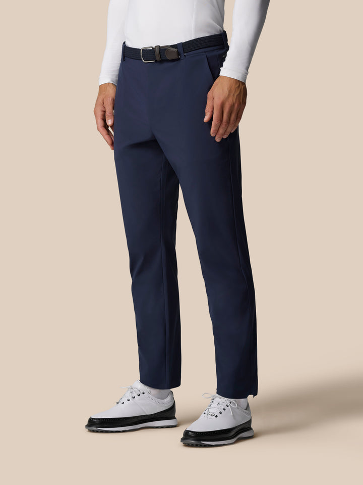 Lower body shot of a model wearing navy Golf Pinnacle Winter Trousers with a black belt and white shoes
