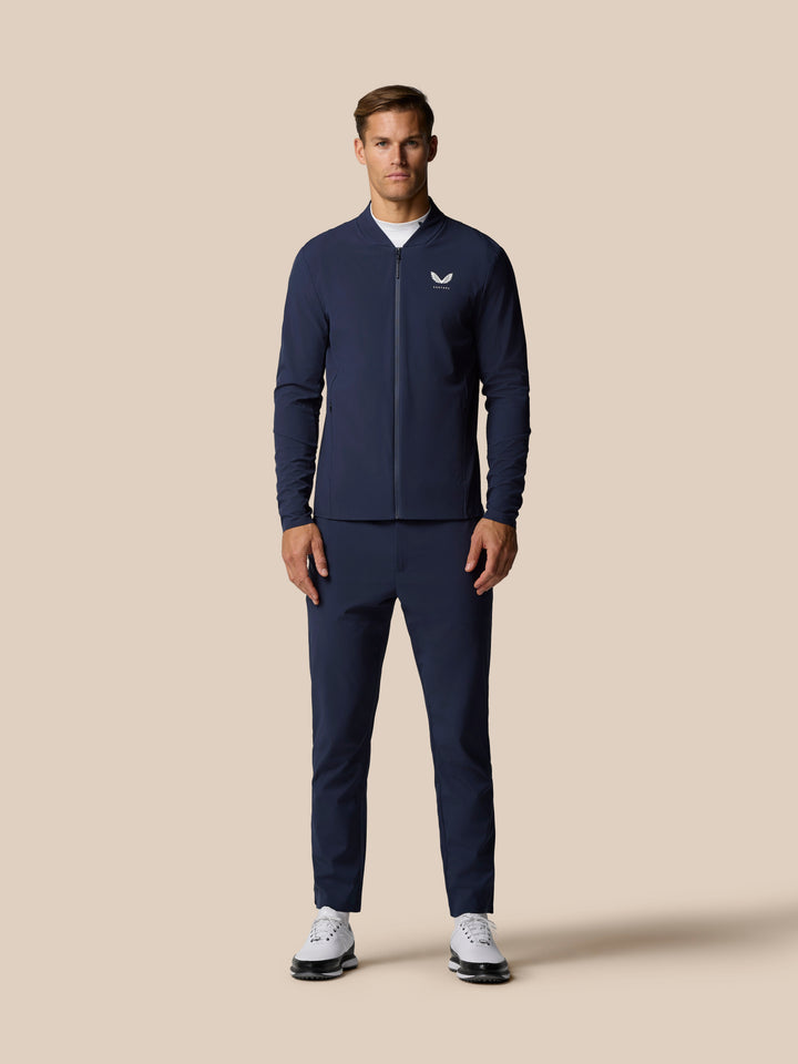 Male model wearing navy zip bomber jacket with Castore logo on chest against a beige backdrop
