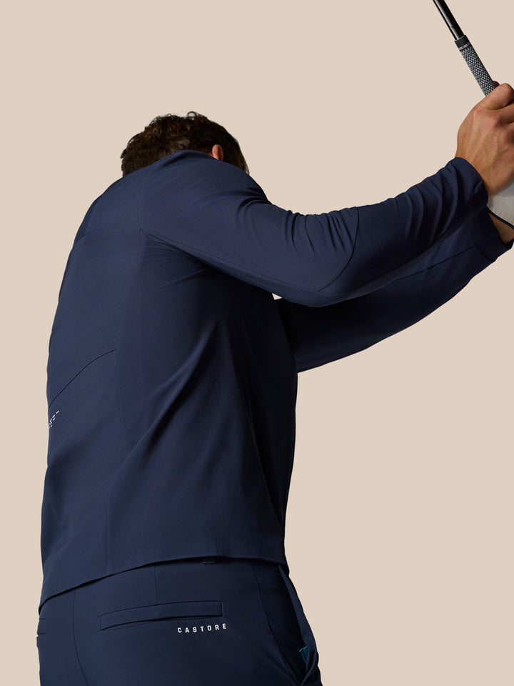 Back view of a golfer in navy Castore winter kit raising a golf club overhead