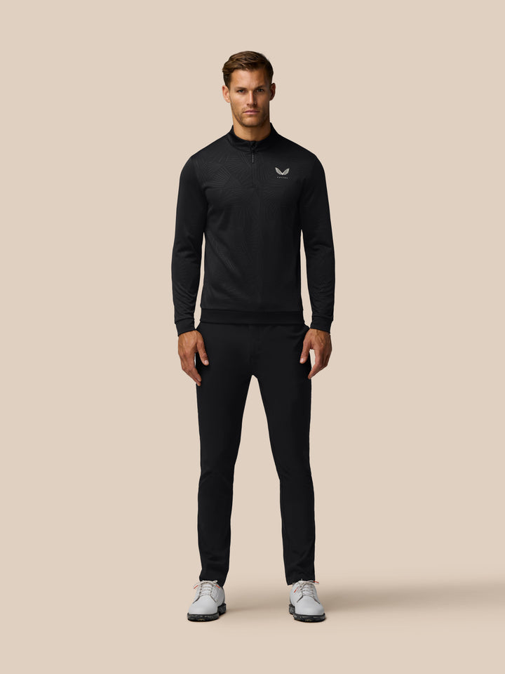 Male model in full length view wearing black Golf Club Classic 1/4 Zip Debossed Top with subtle print against a beige background