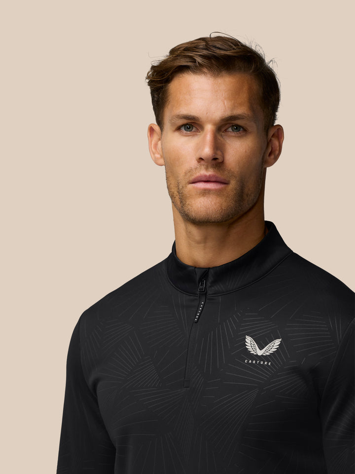Close up of the chest area on a black quarter zip golf top showing all over print and Castore wing logo.