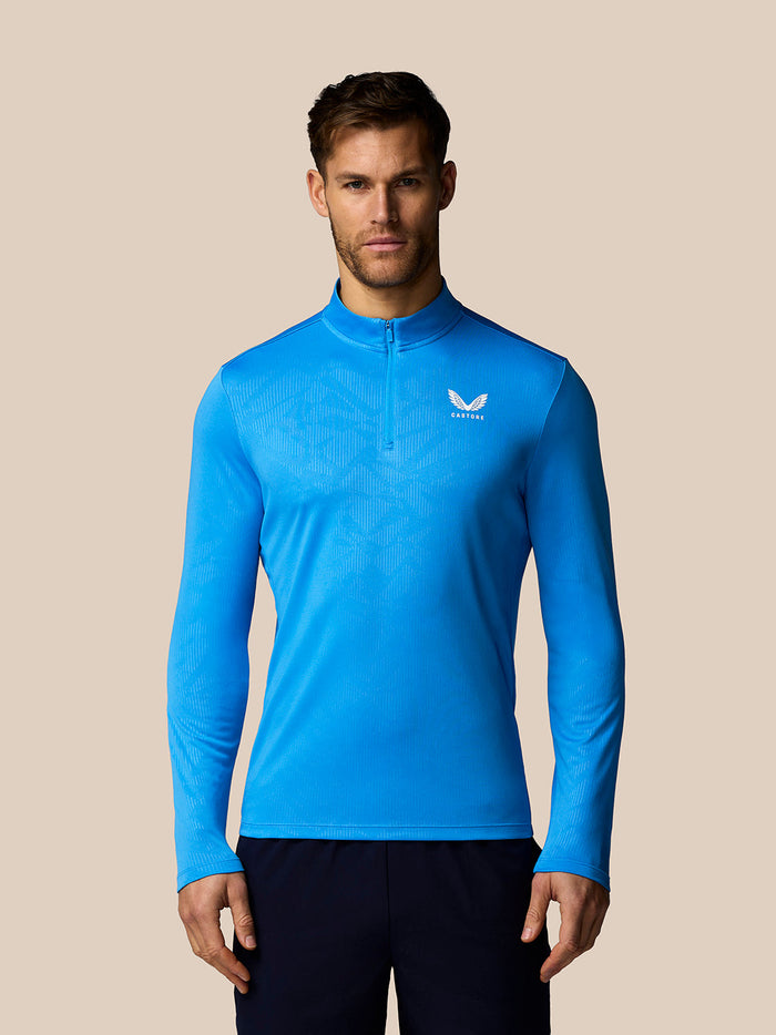Man wearing a blue long-sleeve athletic shirt with a logo on a beige background